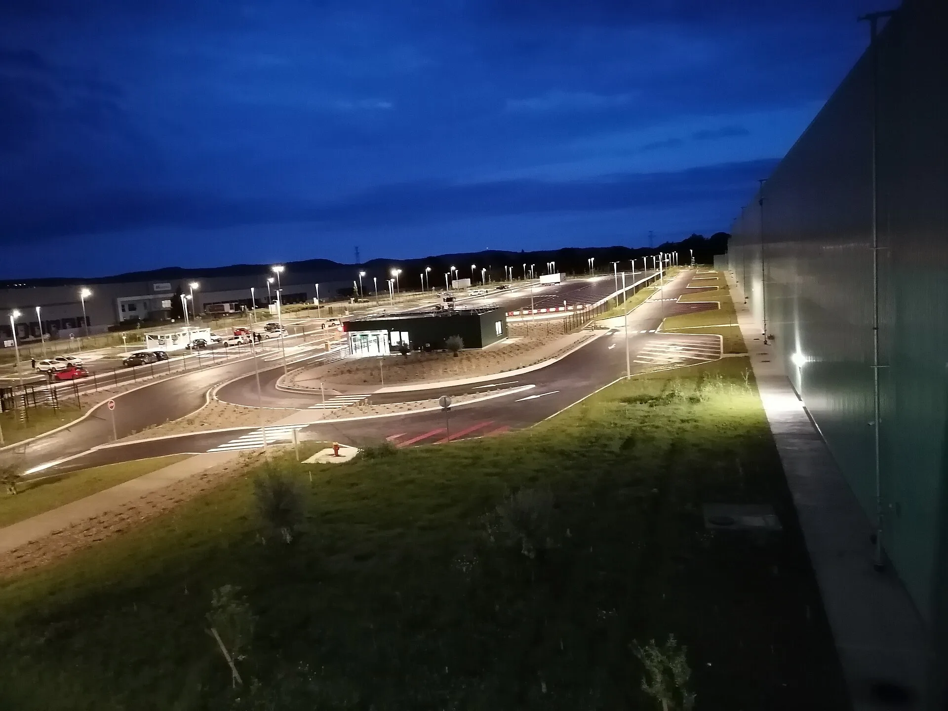 Vue depuis la salle de pause de l'entrepôt Intermarché sur le poste de garde de l'entrepôt Intermarché et l'entrepôt Nespresso plus au fond.