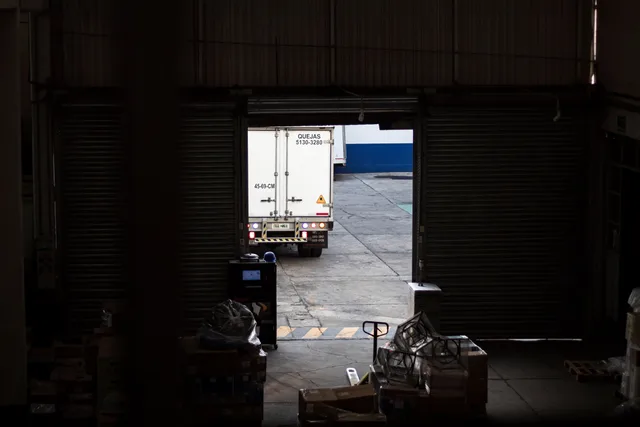 A white delivery truck exits a dimly lit warehouse loading dock, surrounded by packages and pallets. Receiving and putaway technology